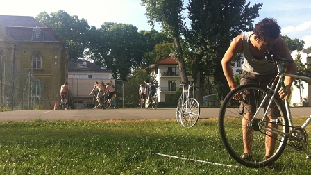 Ein Bike-Polo-Spieler bei seinem Rad auf der Wiese, während im Hintergrund das erste Spiel beginnt